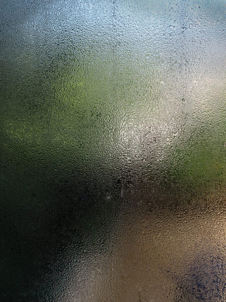 Textured view through a foggy glass, showing blurred greenery in the background.